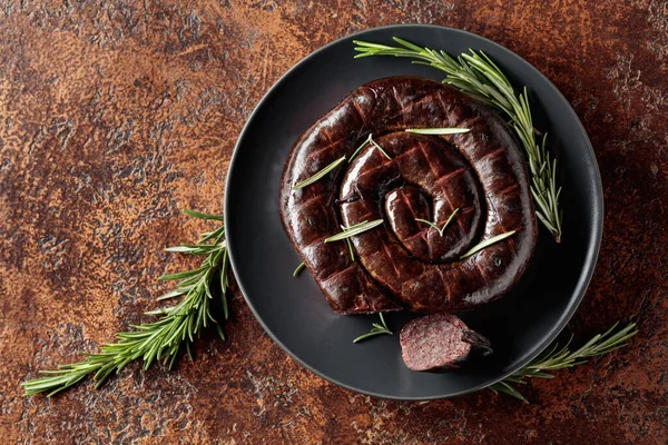 Black pudding or blood sausage with rosemary on a black plate. Top view. Copy space.