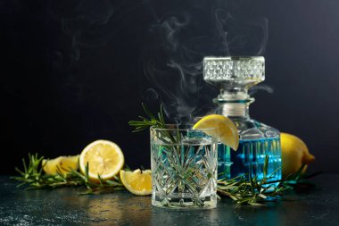 Kristal bardakta limon ve biberiyeli kokteyl cin toniği. Masada tütsülenmiş biberiye eski moda kokteyl..