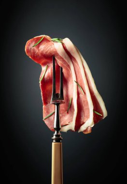Sliced prosciutto with rosemary on a fork.
