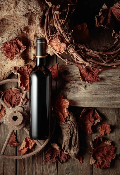 Bottle of red wine on a vintage rustic background with old wood and dried-up vine leaves. Concept of old wine.