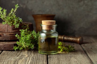 Bottle of thyme essential oil with fresh thyme twigs on an old wooden table.