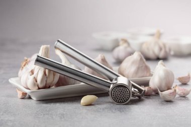 Garlic and garlic press on a grey stone table.
