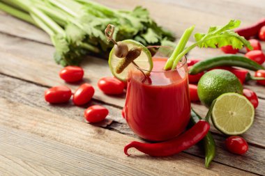 Salatalık, zeytin, limon ve kereviz ile süslenmiş Bloody Mary kokteyli. Eski ahşap bir masada malzemelerle domates suyu..
