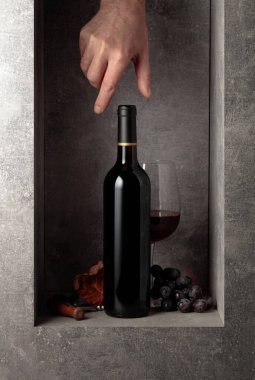 Bottle of red wine with grapes. Hand reach for a bottle of wine.