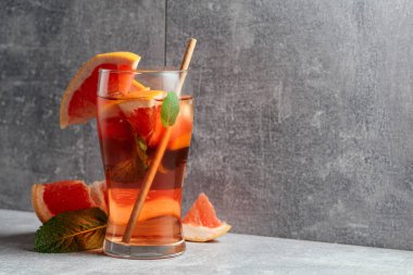 Buzlu çay, naneli ve greyfurtlu. Gri arka planda malzemeleri olan soğuk, ferahlatıcı bir içecek. Boşluğu kopyala.