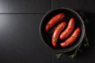 Eski siyah bir tavada biberiyeli kızarmış Bavyera sosisi. Boşluğu kopyala.