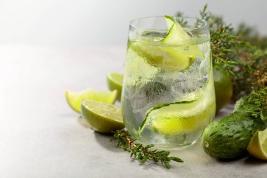 Beyaz taş bir masada buz, limon, salatalık ve ardıç dallı kokteyl cin toniği. Soğuk serinletici içecek, sisli bardaktaki doğal buzla birlikte..