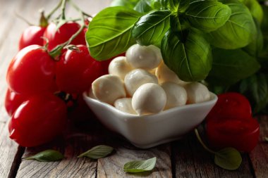 Eski ahşap bir masada fesleğenli ve domatesli Mozzarella peyniri. Geleneksel İtalyan atıştırması.