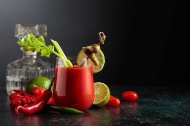 Salatalık, zeytin, limon ve kereviz ile süslenmiş Bloody Mary kokteyli. Siyah arka planda malzemelerle domates suyu. Boşluğu kopyala.