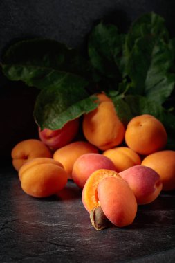 Apricots with leaves on a black stone table.