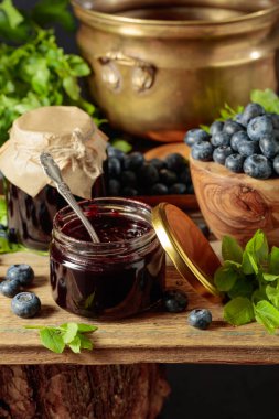 Eski ahşap bir masada yaban mersini reçeli bulunan küçük kavanozlar..