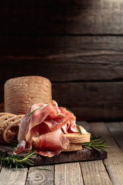 Prosciutto with bread and rosemary on an old wooden table. Copy space.