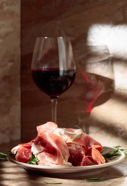 キッチンテーブルの上にローズマリーと赤ワインとイタリアのProsciuttoまたはスペインのジャモン — ストック写真