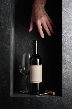Eski boş etiketli bir şişe kırmızı şarap için elini uzat. Pahalı şarapların teması üzerine bir konsept resim.