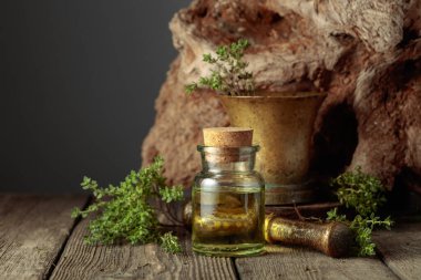 Bottle of thyme essential oil with fresh thyme twigs on an old wooden table. Copy space.