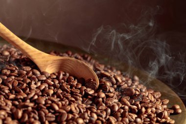 Orta pişmiş kahve çekirdekleri kızartma tavasında dumanlıdır. Boşluğu kopyala.