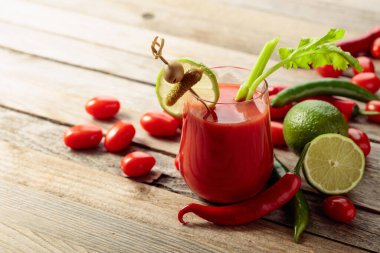 Salatalık, zeytin, limon ve kereviz ile süslenmiş Bloody Mary kokteyli. Eski ahşap bir masada malzemelerle domates suyu..