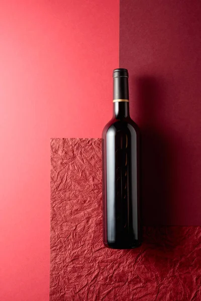 Kırmızı Arka Planda Bir Şişe Kırmızı Şarap Farklı Dokular Gölgelerle — Stok fotoğraf