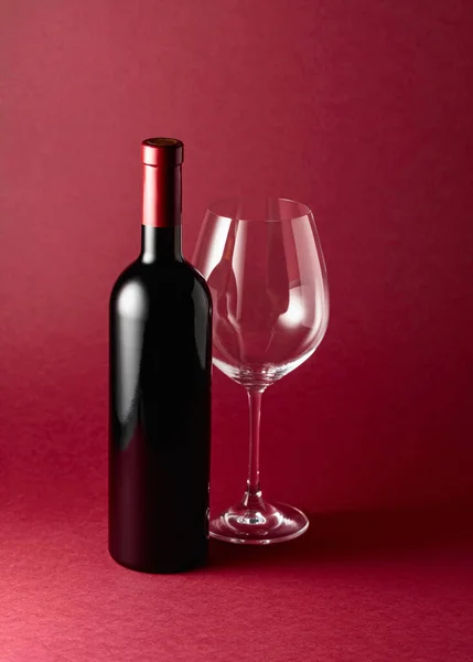 Fles Rode Wijn Een Leeg Glas Een Rode Achtergrond Kopieerruimte — Stockfoto