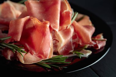 Italian prosciutto or Spanish jamon with rosemary on a black plate.