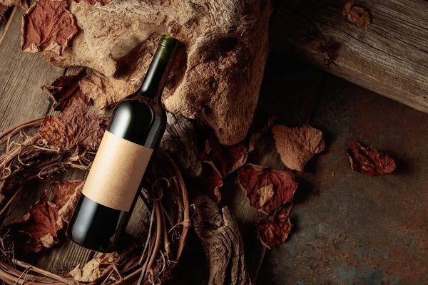 Bottle of red wine with a blank old label. Vintage rustic background with old wood and dried-up vine leaves. Concept of old wine.