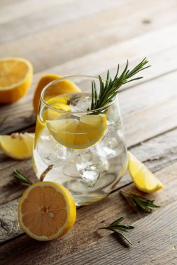 Buzlu cin toniği, biberiye ve buzlu bardakta limon dilimleri. Eski ahşap bir masanın üzerinde malzemeleri olan kokteyl. Boşluğu kopyala.