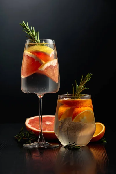 用冰块 迷迭香 橙子和柚子装饰在结冰的玻璃杯中的生姜补品 杯子上的鸡尾酒在黑色木制桌子上 复制空间 — 图库照片