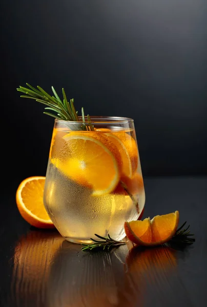 用冰块 迷迭香和橙子装饰在结冰的玻璃杯里 黑色木制桌子上的鸡尾酒玻璃杯 — 图库照片