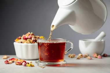 Bitki çayı bardağa dökülür. Kurumuş otlar ve çiçekler taş masaya saçılmış..