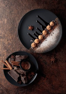 Çikolatalı trüf mantarı, siyah tabakta, çikolata soslu. Tatlılar kakao tozu ve pudra şekeriyle serpiştirilir..