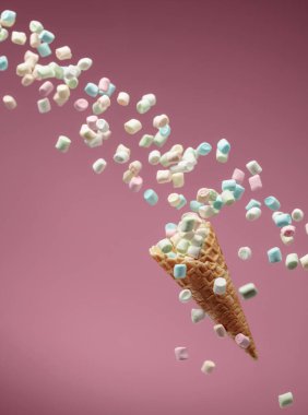 Küçük renkli marşmelovlar pembe bir arka planda waffle külahına düşer. Boşluğu kopyala.