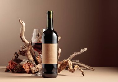 Eski ahşap karışımlı bir şişe ve bir bardak kırmızı şarap. Ürün markalaşma, kimlik ve ambalaj için bej arka planda minimal kompozisyon. Boşluğu kopyala.