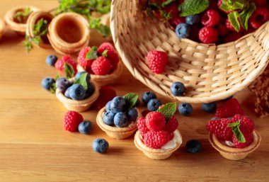 Küçük tartlar taze ahududu ve böğürtlenlerle süslenmiş ahşap bir masada nane ile.