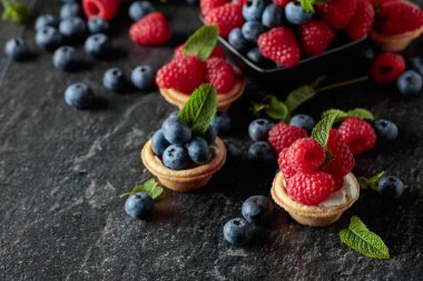 Siyah arka planda naneli taze ahududu ve yaban mersinli küçük tartlar..