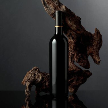 Siyah yansıtıcı arka planda bir şişe kırmızı şarap. Arka planda eski yıpranmış bir pürüz var. Metnin için alanı olan ön görünüm.