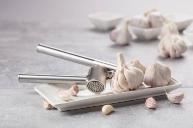 Garlic and garlic press on a grey stone table.