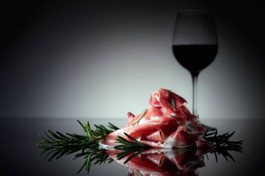 Italian prosciutto or Spanish jamon with rosemary and red wine on a black background.