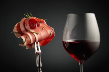 Kırmızı şarap ve biberiyeli dilimlenmiş jambon, siyah arka planda..