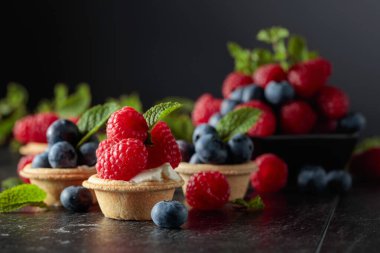 Siyah arka planda naneli taze ahududu ve yaban mersinli küçük tartlar..