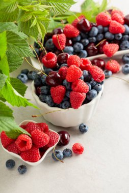 Beyaz bir masada yapraklı böğürtlenler. Renkli yabanmersini, ahududu ve tatlı kiraz karışımı..
