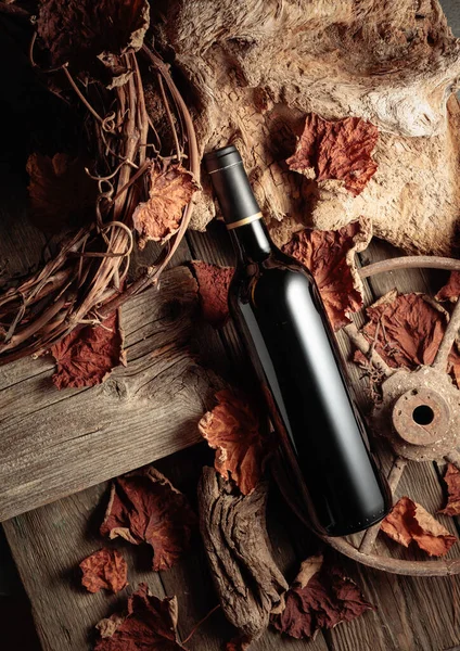 Bottle of red wine on a vintage rustic background with old wood and dried-up vine leaves. Concept of old wine.