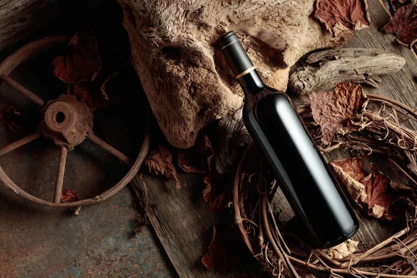 Bottle of red wine on a vintage rustic background with old wood and dried-up vine leaves. Concept of old wine. Copy space.