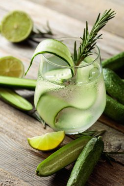 Buzlu cin toniği, biberiye, limon ve buzlu bardakta salatalık dilimleri. Eski ahşap bir masada malzemelerle kokteyl.. 