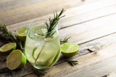 Buzlu cin toniği, biberiye ve buzlu bardakta limon dilimleri. Eski ahşap bir masanın üzerinde malzemeleri olan kokteyl. Boşluğu kopyala.