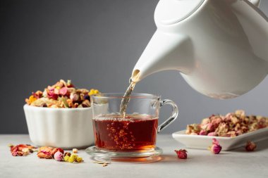 Bitki çayı bardağa dökülür. Kurumuş otlar ve çiçekler taş masaya saçılmış..