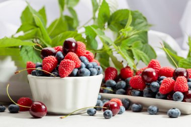 Beyaz bir masada yapraklı böğürtlenler. Renkli yabanmersini, ahududu ve tatlı kiraz karışımı..