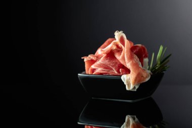 Siyah yansıtıcı arka planda biberiyeli Prosciutto. Boşluğu kopyala.