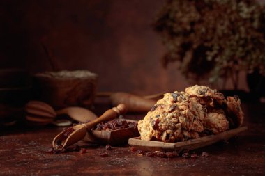 Kahverengi bir masada yulaf ezmeli kuru üzümlü kurabiye ve mutfak aletleri. Boşluğu kopyala.