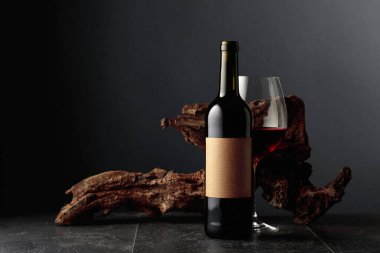 Boş etiketli bir şişe ve bir bardak kırmızı şarap. Arka planda eski yıpranmış bir pürüz var. Kopyalama alanı ile ön görünüm.