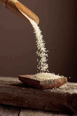 Tahta tabakta tahtadan bir kaşıkla beyaz susam taneleri dökülüyor. Boşluğu kopyala.